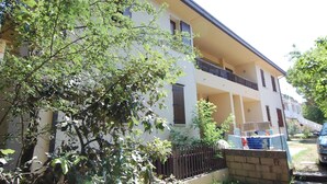 A two-story building with a balcony, a stone wall, and a parked car. - Sun Drenched Seaside Holiday Home near Venice (Rosolina)