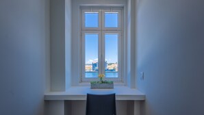 Ein Zimmer mit Fensterblick auf ein Gewässer, einem weißen Schreibtisch und einem Stuhl.