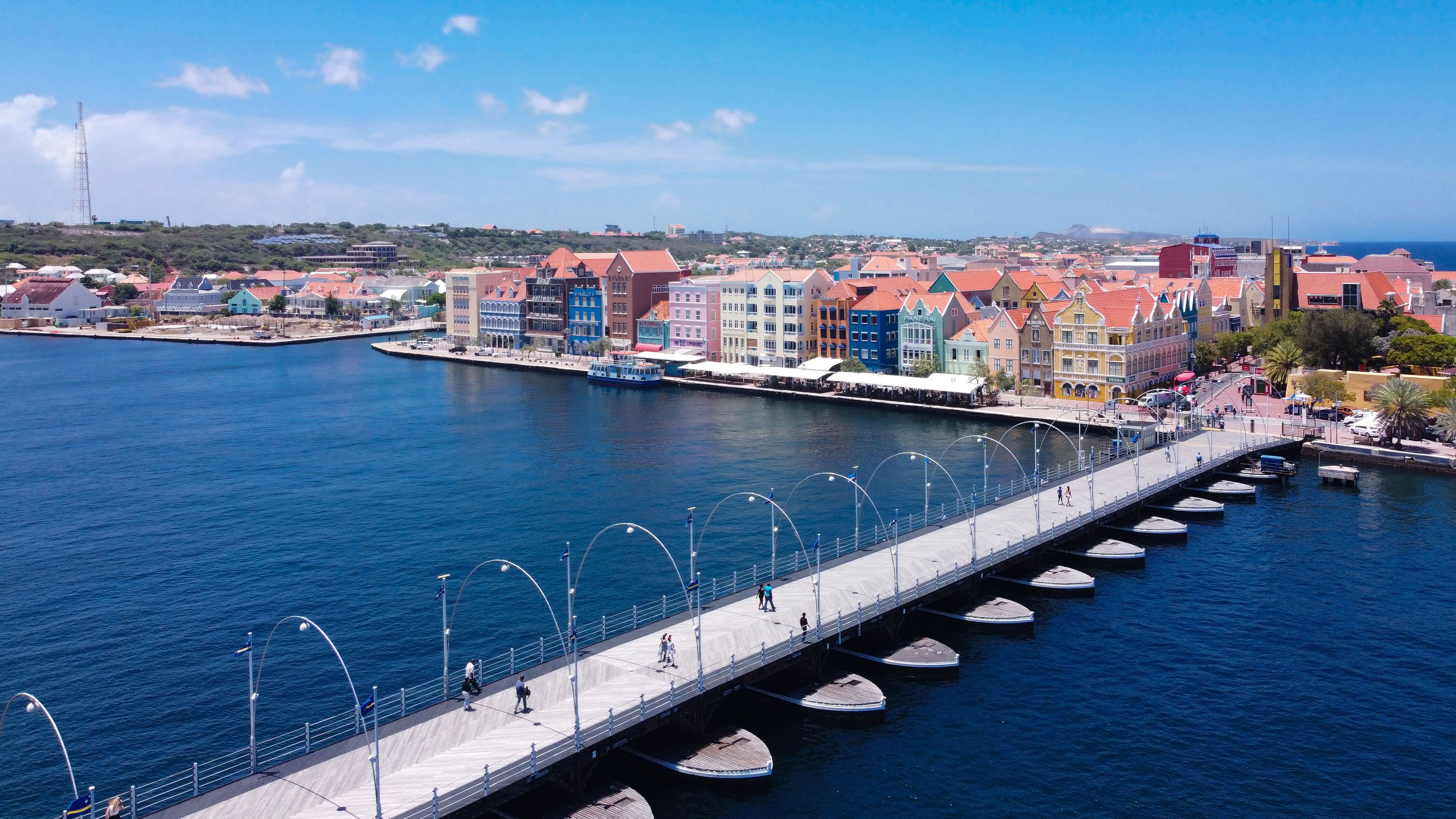 Une promenade en bord de mer, bordée de bâtiments aux couleurs vives, avec un pont et des bateaux amarrés le long du quai.