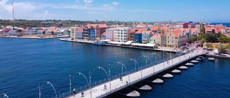 Une promenade en bord de mer, bordée de bâtiments aux couleurs vives, avec un pont et des bateaux amarrés le long du quai.
