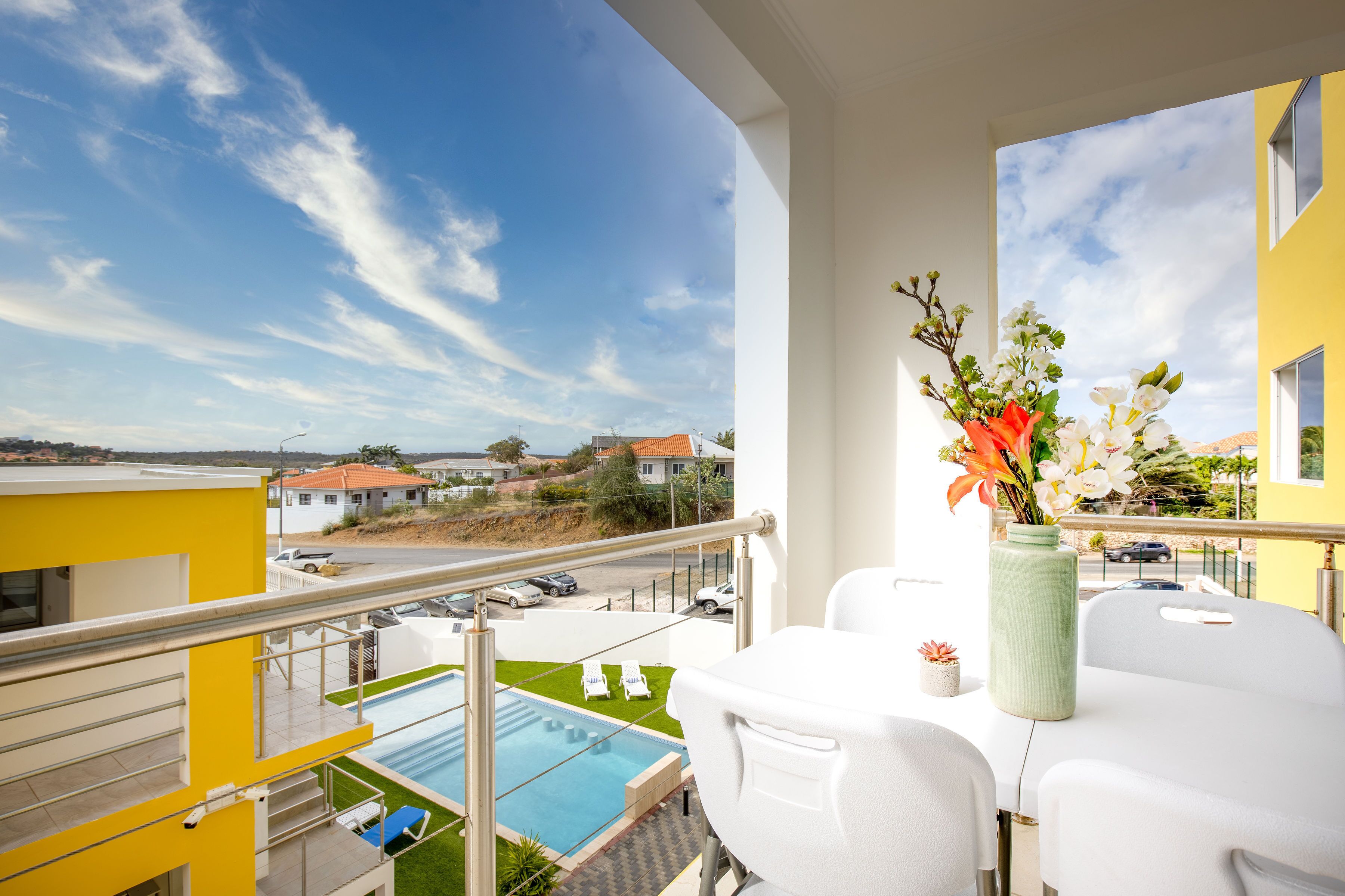 A balcony with a pool, white furniture, and a vase of flowers.