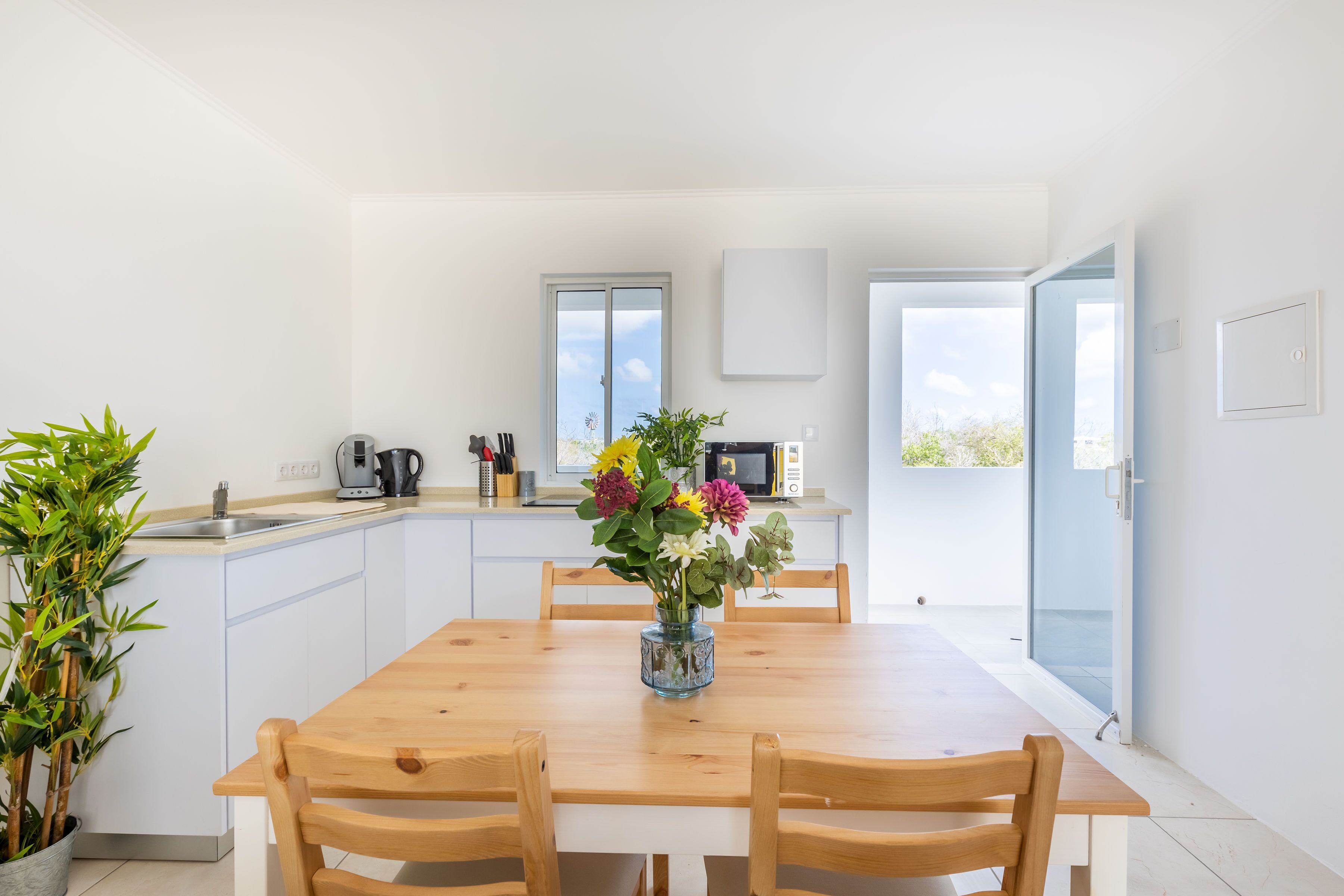 Una cocina moderna con armarios blancos, una mesa de comedor de madera y un jarrón con flores.