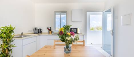 Una cocina moderna con armarios blancos, una mesa de comedor de madera y un jarrón con flores.