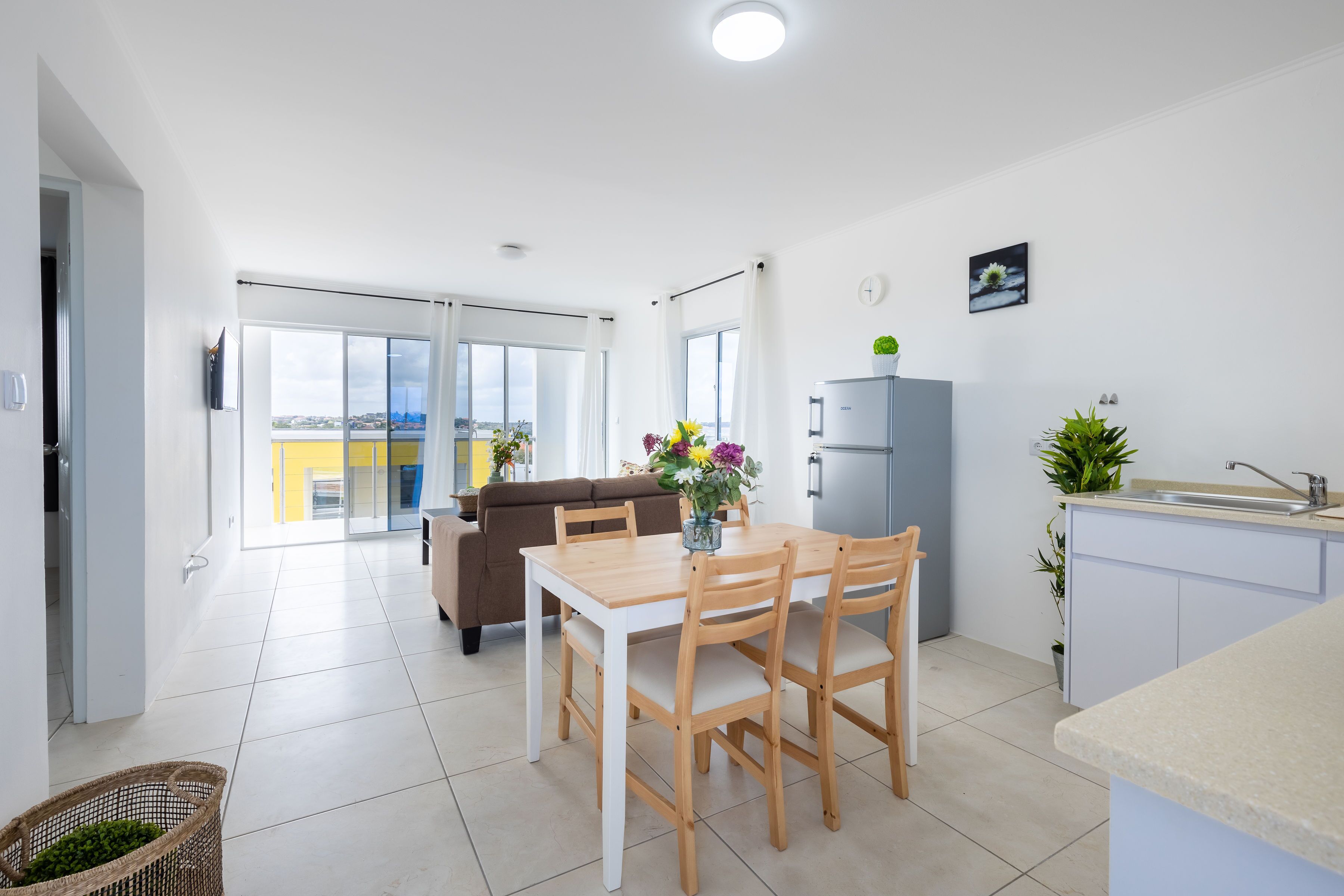 A modern kitchen with a dining area, a refrigerator, and a view of the city.