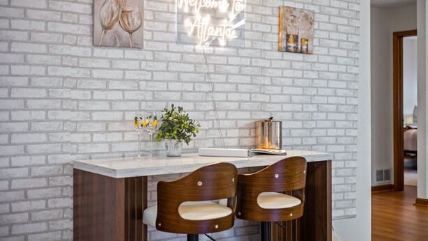 A reception area with a white brick wall, a neon sign reading "Welcome to Atlanta," two wooden chairs, a small plant, and a decorative item on the counter. - Ultimate Stone Mountain I Cabin-Style I  Sleep 20 (Stone Mountain)