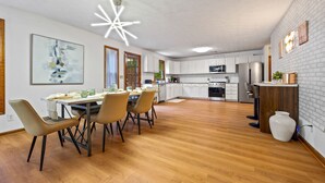 A modern kitchen with white cabinets, a dining area with a wooden table and chairs, and a bright ceiling light. - Ultimate Stone Mountain I Cabin-Style I  Sleep 20 (Stone Mountain)