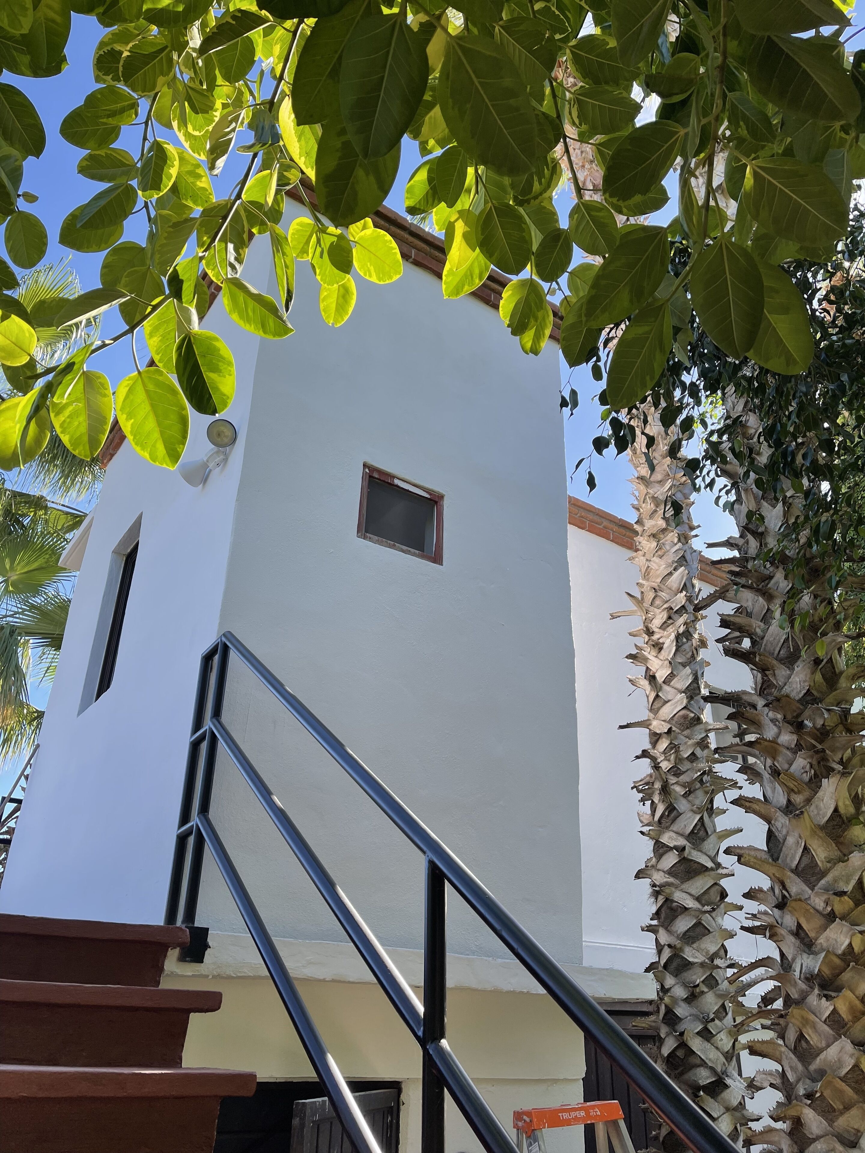 Un edificio blanco con una ventana pequeña y una escalera metálica que lleva a una puerta.