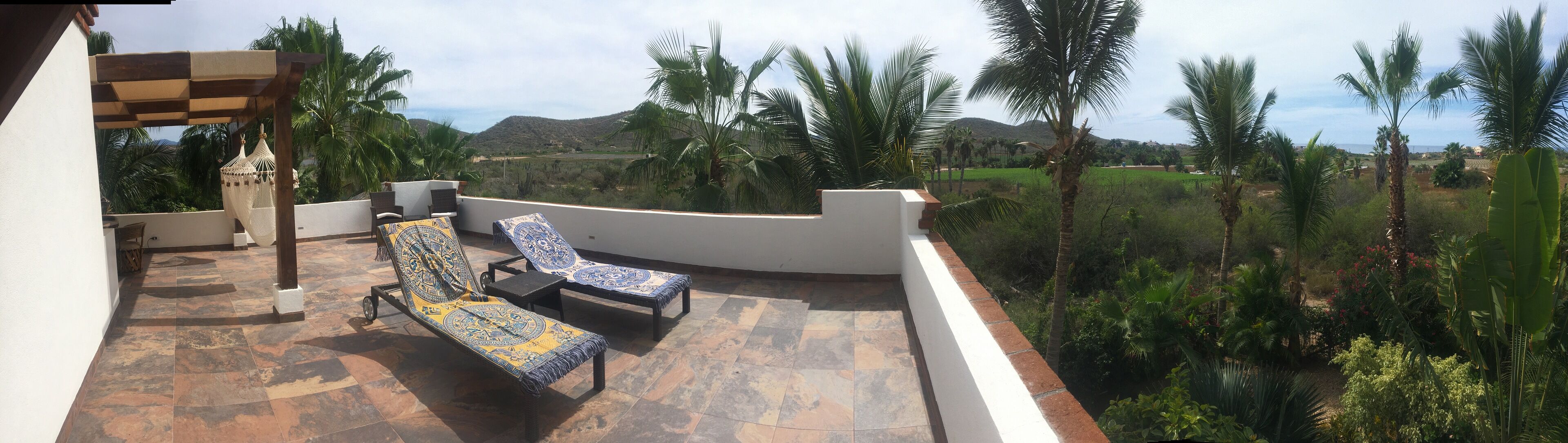 A terrace with two sun loungers, a hammock, and a view of a green landscape with palm trees and hills.