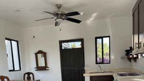 Una cocina con comedor, ventilador de techo, una puerta negra y ventana con vistas a follaje.