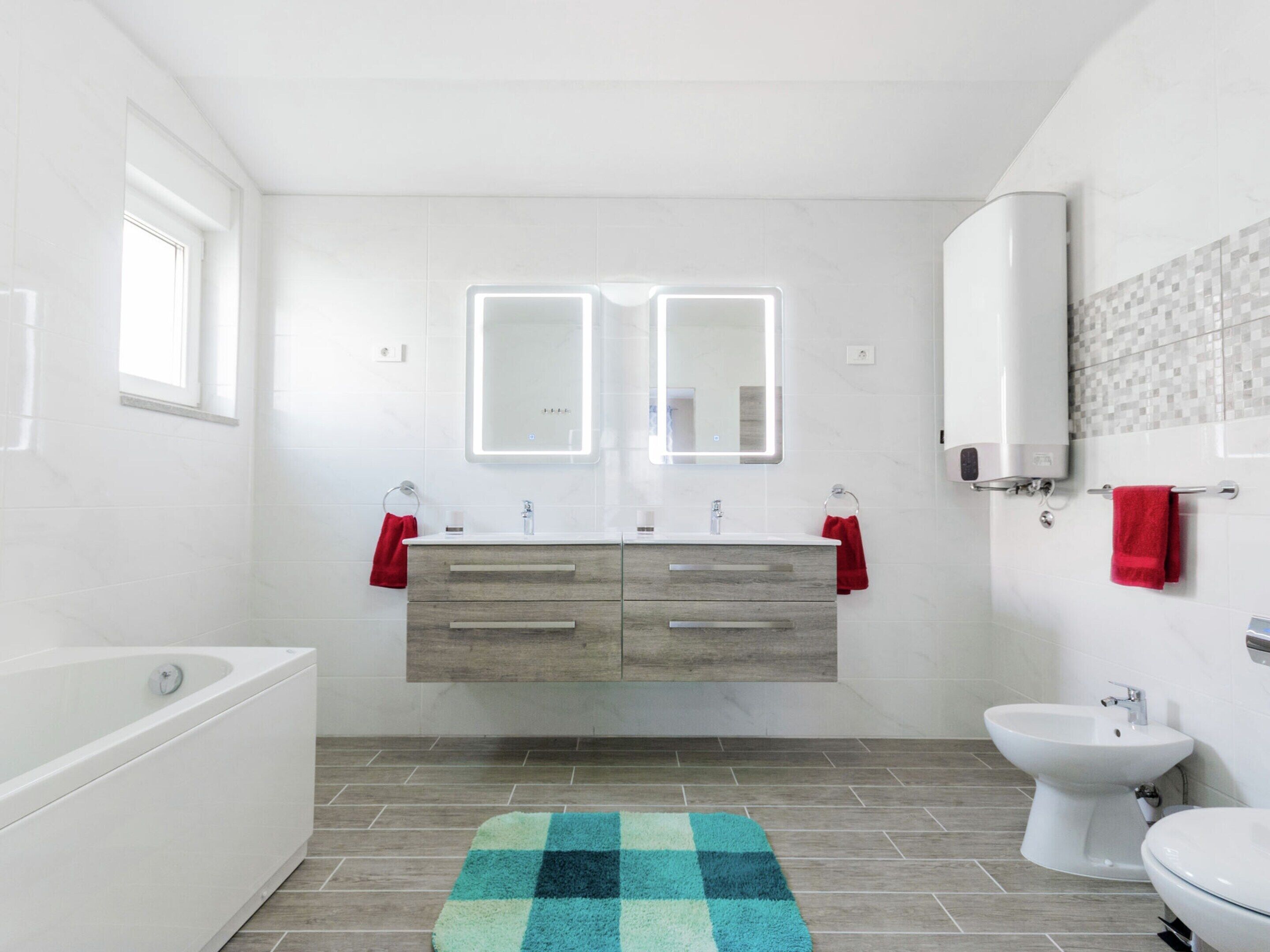 Ein modernes Badezimmer mit einer Badewanne, einem Doppelwaschbecken mit zwei Spiegeln, einer Toilette und einem Bidet.