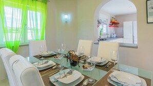 Comedor con una mesa de vidrio dispuesta para seis comensales, sillas blancas y vista a la cocina a través de un arco.