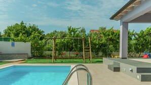 Una piscina con una escalera de metal y un columpio de madera en un área ajardinada.