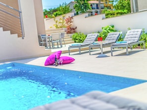 A pool area with lounge chairs and a table, surrounded by a low wall and greenery. - Modern Villa in Salakovci With Private Pool (Labin)