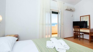 A hotel room with a bed, a desk with a chair, a television, and an air conditioning unit. - Charming Seaside Apartment (Omis)