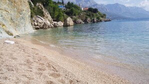 A coastal beach with rocky cliffs, clear water, and mountains in the background. - Charming Seaside Apartment (Omis)