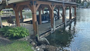 Une terrasse en bois avec des sièges d’extérieur et un barbecue, donnant sur une étendue d’eau calme.