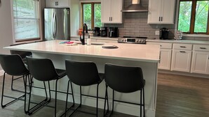 Une cuisine moderne dotée d’un grand îlot central, de tabourets de bar, de meubles blancs, d’un réfrigérateur en acier inoxydable et d’un mur de fond en briques.