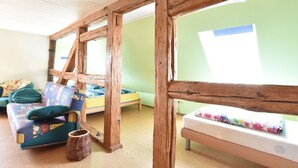 Egy szoba, melynek a jellemzői: rusztikus, fa borítású mennyezet, zöld színű fal, mintás párnákkal díszített kanapé és virágmintás takaróval borított ágy.