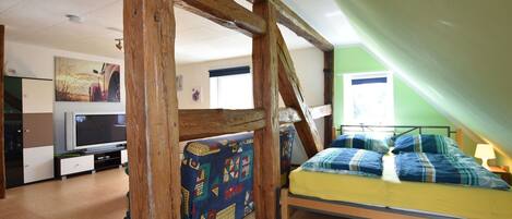 A bedroom with a bed, a TV, a wooden beam structure, and a window.