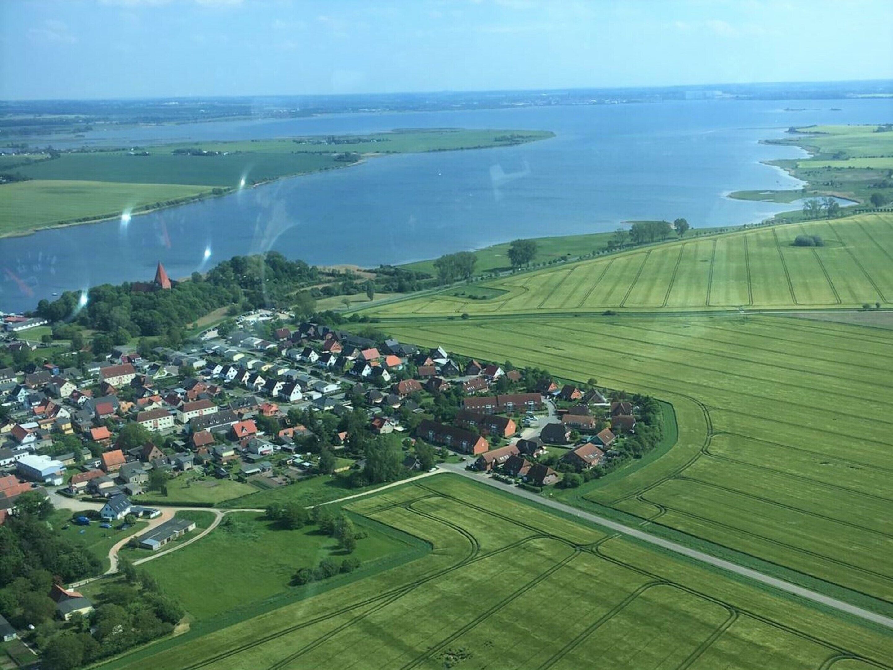 An aerial view of a small town with a river, green fields, and a church.