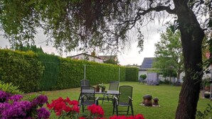 A garden with a table and chairs, surrounded by hedges and flowering plants. - Apartment near Insel Poel (Blowatz)
