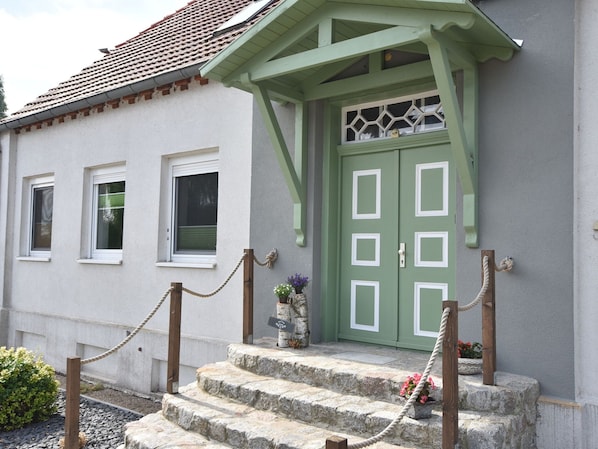 Un bâtiment avec une porte verte, des fenêtres à cadre blanc et des marches en pierre menant à l’entrée.