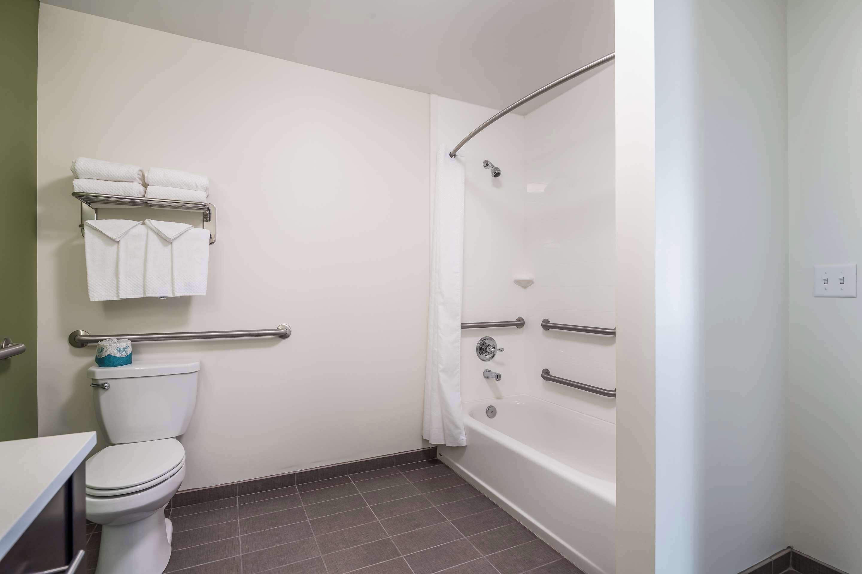 Ein Badezimmer mit Toilette, einer Badewanne mit Haltegriffen und einem Handtuchhalter mit gefalteten Handtüchern.