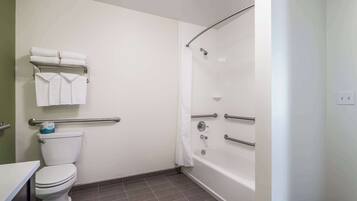 A bathroom with a toilet, a bathtub with grab bars, and a towel rack with folded towels.