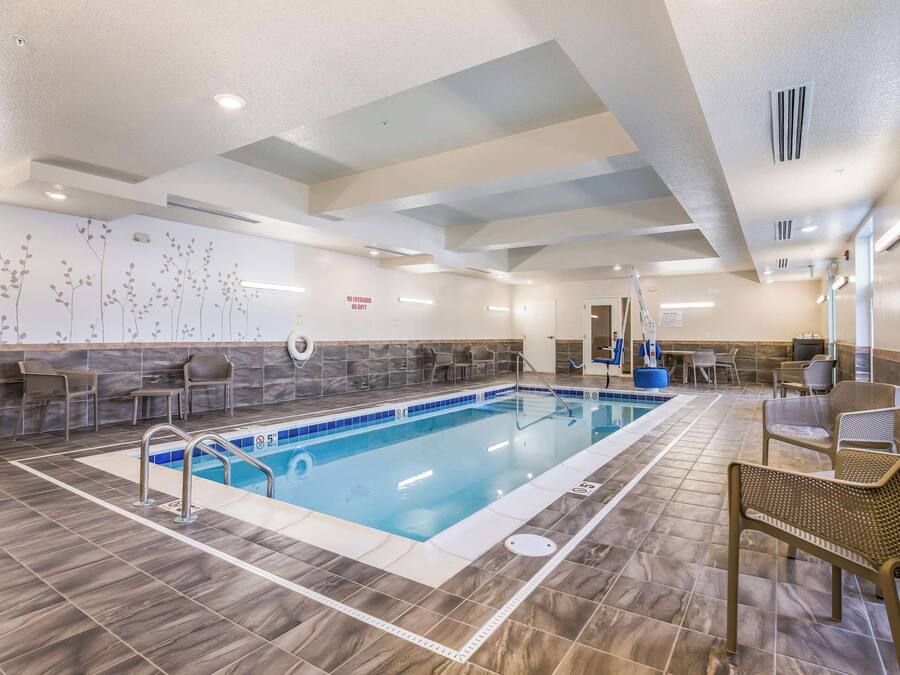 Una piscina con solárium de baldosas, sillas de descanso y una pared con motivos florales.