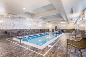 A swimming pool with a tiled deck, lounge chairs, and a wall with a floral pattern.