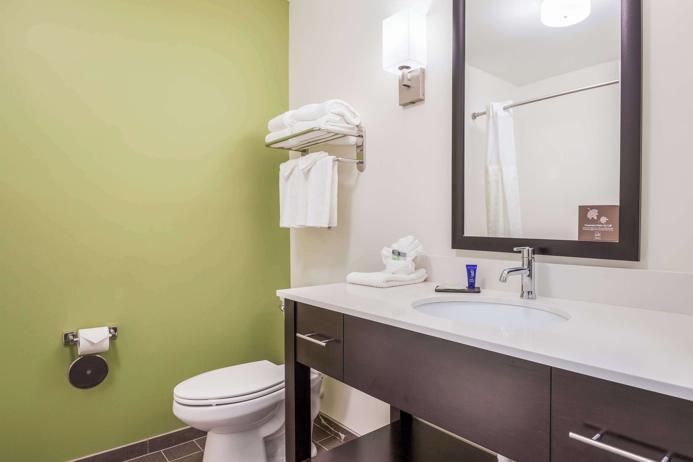 A bathroom with a toilet, a sink, a mirror, and towels on a rack.