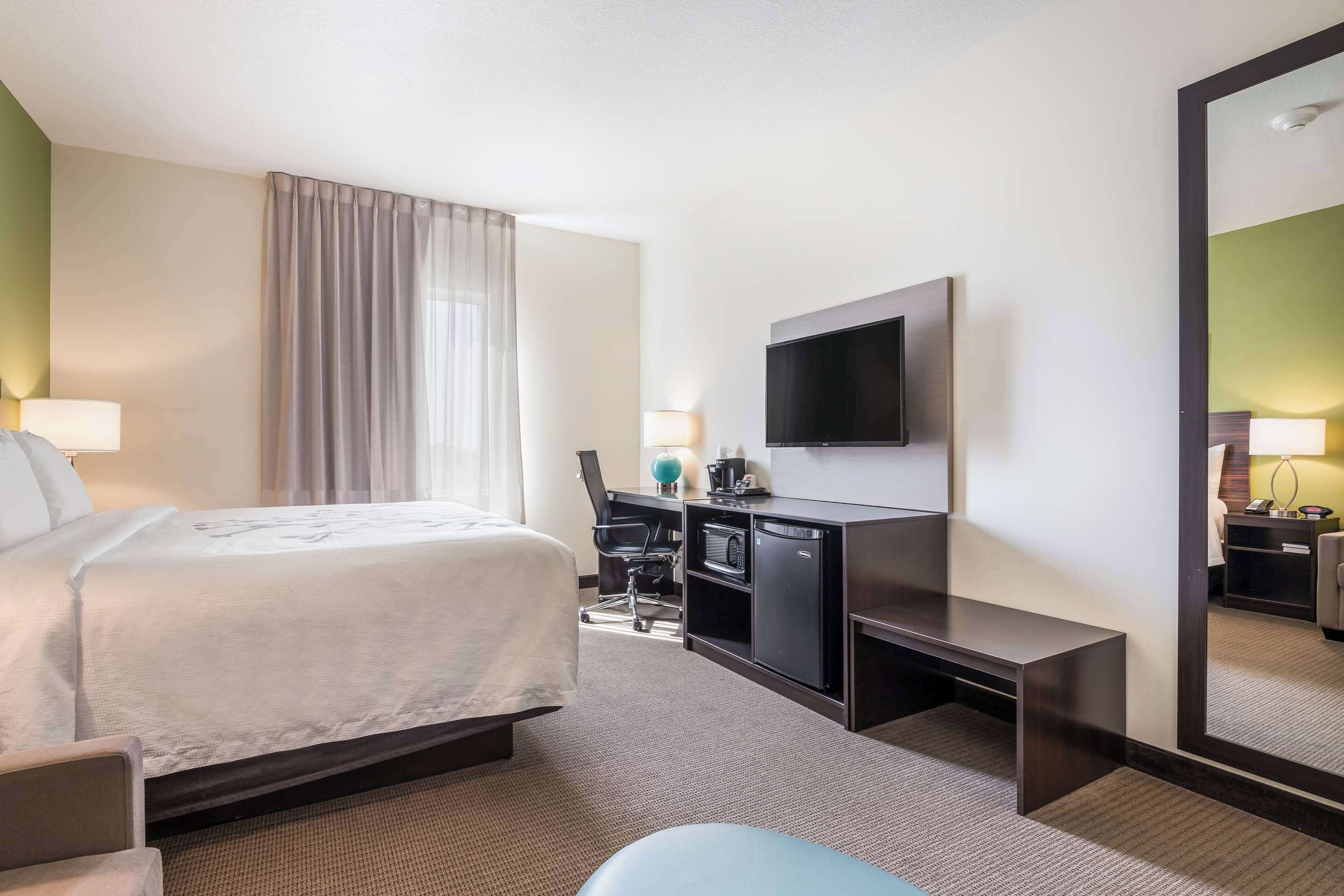 Une chambre d’hôtel avec un lit, un bureau, une chaise et un grand miroir.