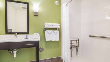 A bathroom with a green wall, a white sink, a mirror, a towel rack, and a shower area.