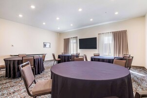 Un salón de conferencias con mesas redondas, sillas, un televisor de pantalla plana y suelo alfombrado.