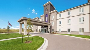 A modern hotel with a flat roof, a central entrance, and a flag in front. - Sleep Inn & Suites Park City - Wichita North (Wichita)