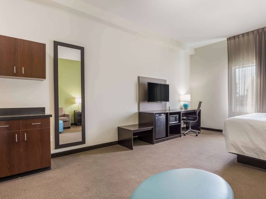 A hotel room with a bed, a desk with a computer, a TV, a wardrobe, and a mirror.