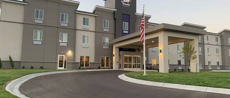 A Sleep Inn & Suites hotel with a modern design, featuring a curved driveway and a well-maintained lawn.