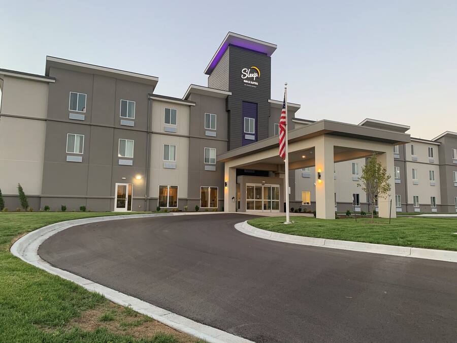 A Sleep Inn & Suites hotel with a modern design, featuring a curved driveway and a well-maintained lawn.