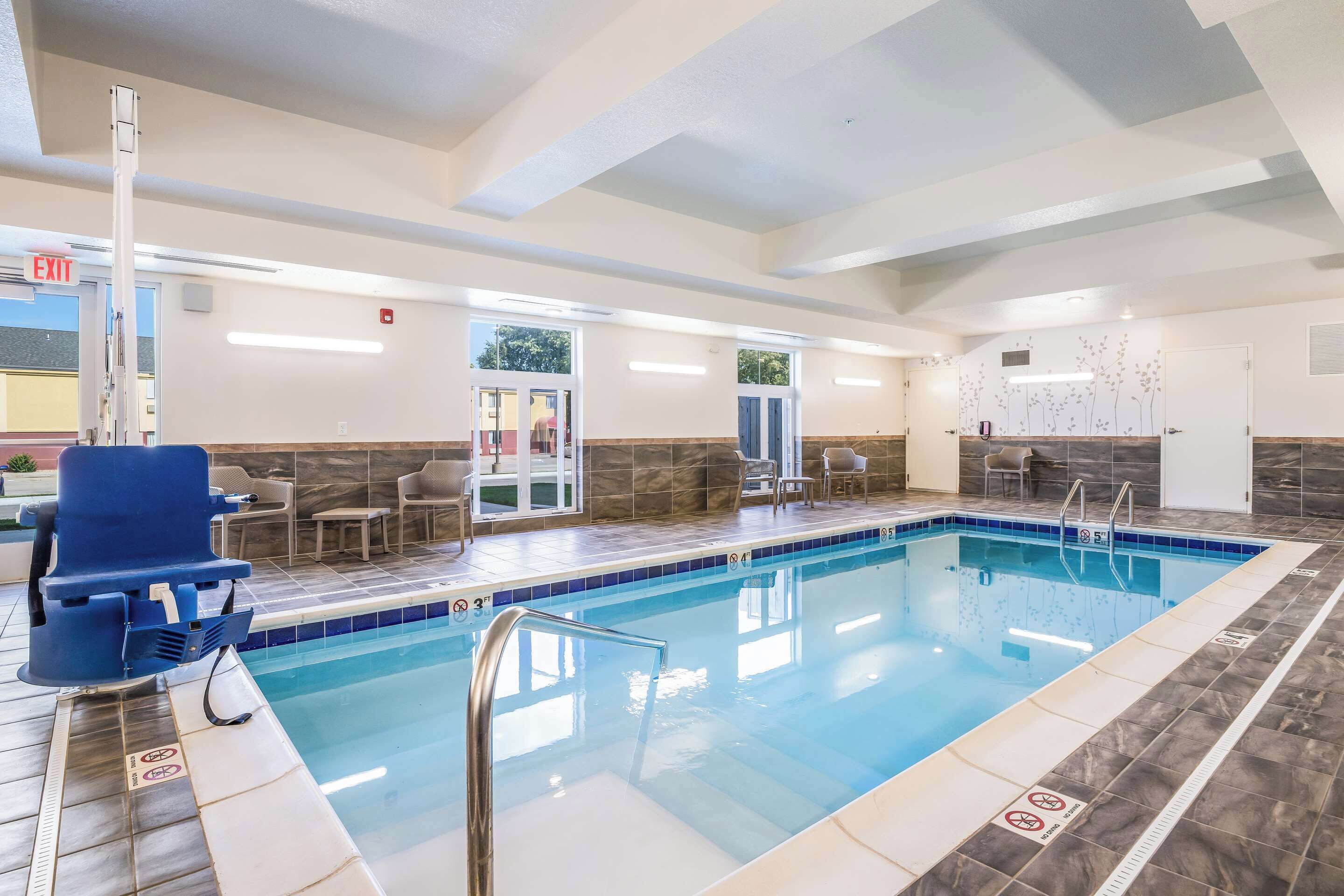 Una piscina interior con agua cristalina, una silla azul y una señal de salida blanca.