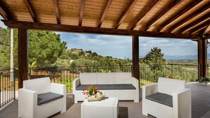 A covered patio with wicker furniture, a table, and a view of a hilly landscape. - Splendid Holiday Home in Castellammare del Golfo near Beach (Castellammare del Golfo)
