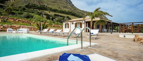 Zona de piscina con sillones de descanso y un edificio al fondo.