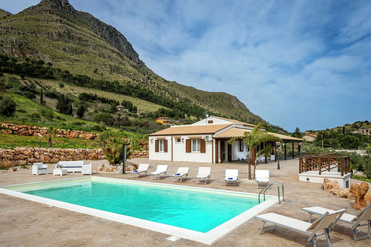 A pool area with lounge chairs and a building with a tiled roof.