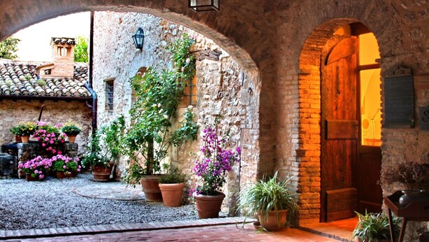 An arched stone courtyard with potted plants, a wooden door, and a lantern. - Scenic Stay in Spoleto (Spoleto)