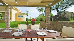 Een buitenterras met een tafel voor zes personen, omringd door stenen zuilen en overdekt met een pergola.