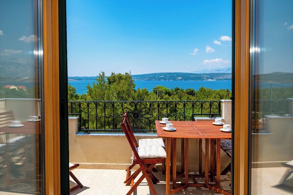 A balcony with a table and chairs, overlooking a body of water and distant mountains. - Apartments Lucija (Novigrad)