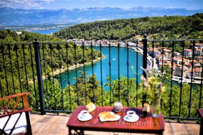 A balcony with a table set for breakfast overlooking a turquoise lake and a mountainous landscape. - Apartments Lucija (Novigrad)