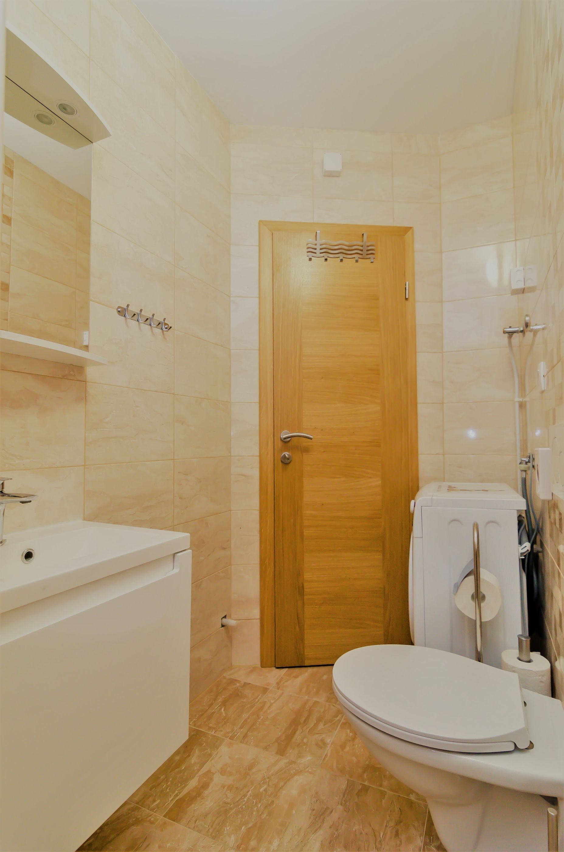 Une salle de bain avec une porte en bois, des toilettes blanches et un lavabo surmonté d’un miroir.