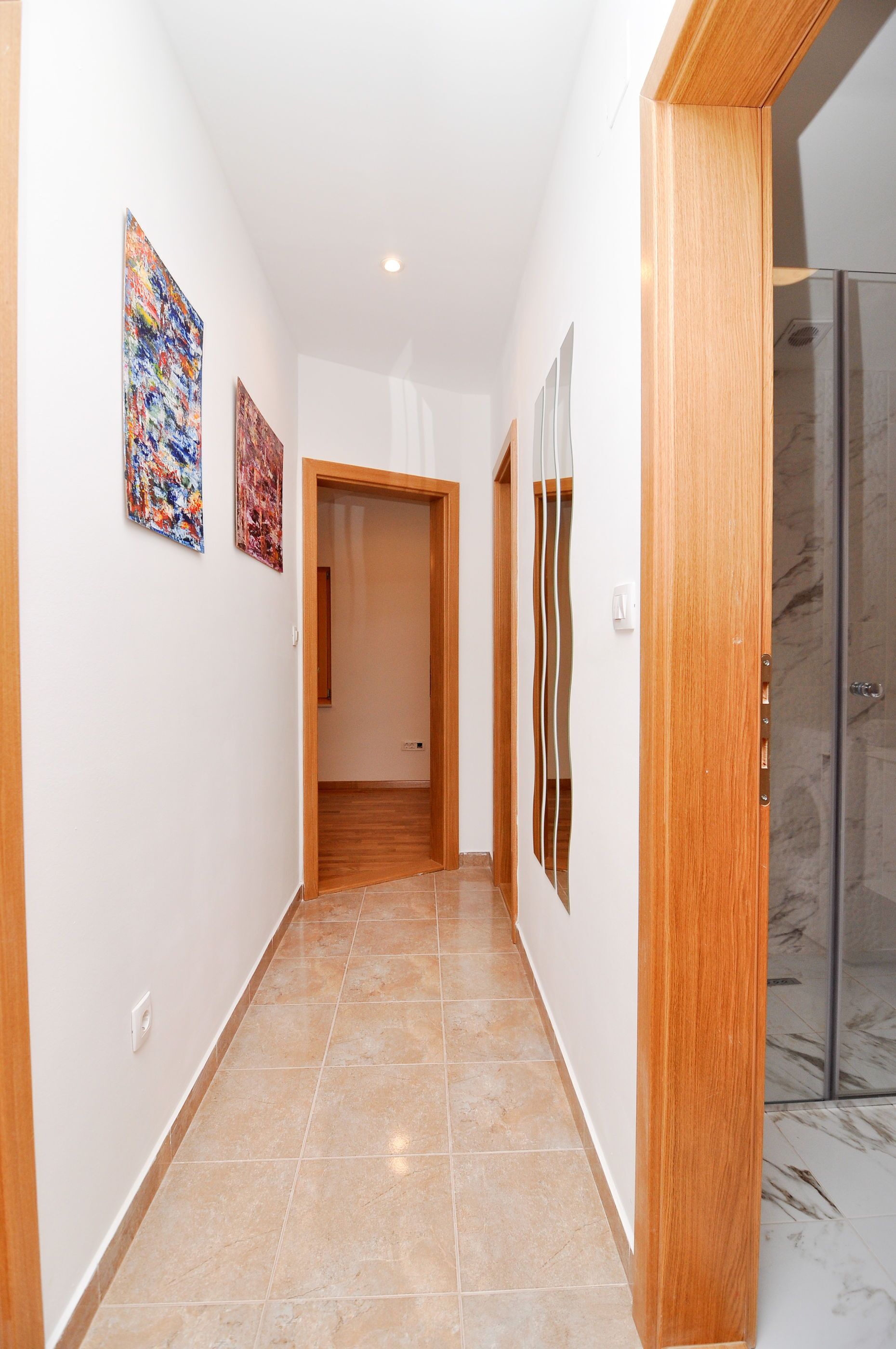 A hallway with tiled flooring, wooden door frames, and artwork on the walls.
