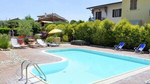 Una piscina rectangular con borde curvo, rodeada por un patio de ladrillo. Se observan sillones de descanso y una sombrilla al fondo.
