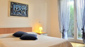 Habitación de hotel con cama, mesita de noche con lámpara, un cuadro en la pared y vistas a través de las cortinas.